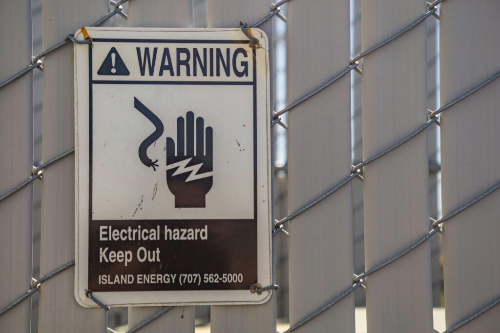 Close-up of a warning sign for electrical hazards on a chain-link fence.