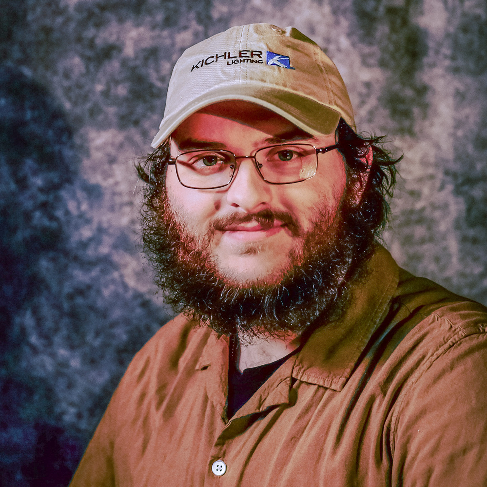 Bryan Guthrie posed for portrait photo in a brown collared shirt with a tan hat, glasses, and beard