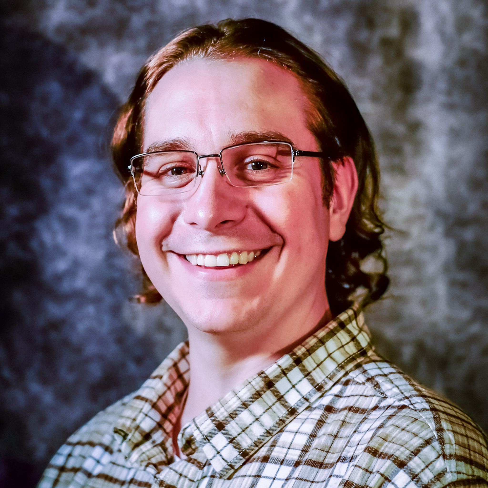 Rush Elliott Jr posed for portrait photo wearing a plaud shirt, glasses, and chin length curly blond hair