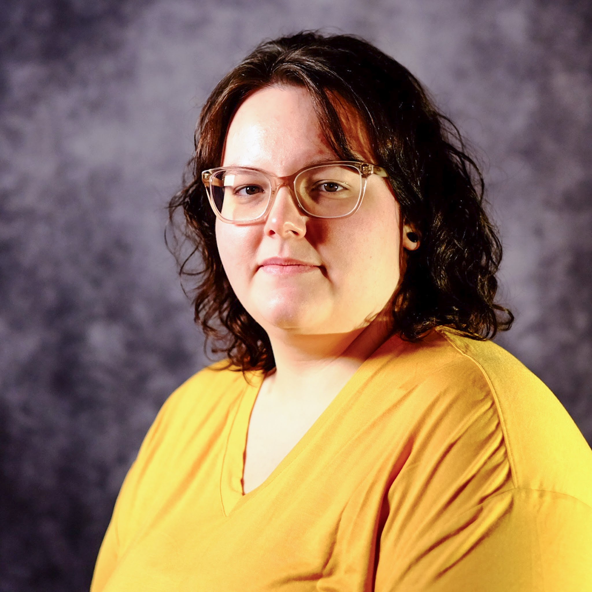 Alexandra Elliott posed for portrait photo in yellow shirt with red, chin length hair and glasses